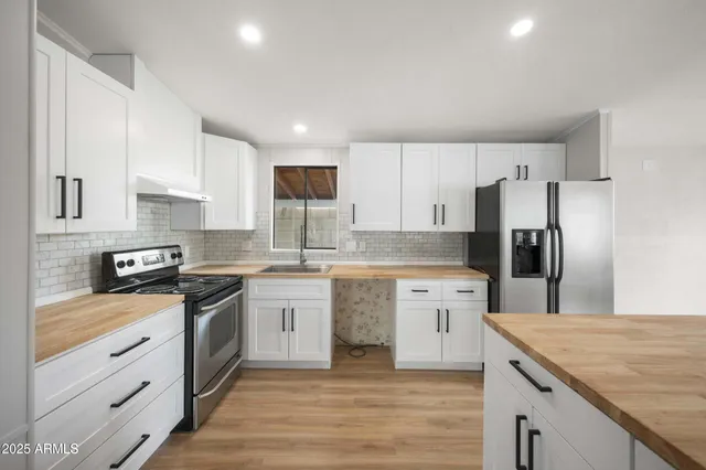 a large kitchen with kitchen island a sink dishwasher a refrigerator and white cabinets with wooden floor