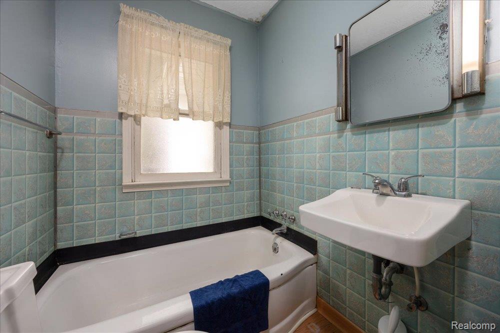 59380 10 Mile Road South Lyon, MI 48178 - Photo 23 of 53 Bathroom featuring aqua square wall tiles, a built-in bathtub, a wall-mounted sink, and a mirrored medicine cabinet with integrated lighting