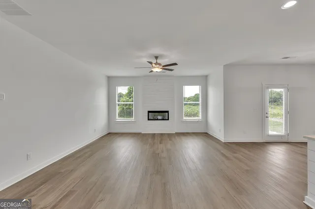 an empty room with wooden floor a ceiling fan and windows