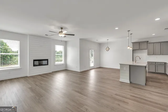 a view of an empty room with wooden floor and a kitchen