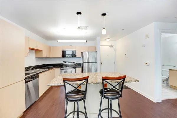 a kitchen with stainless steel appliances kitchen island granite countertop a stove a refrigerator a sink a dining table and chairs with wooden floor