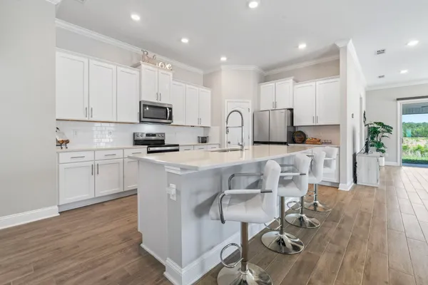 a kitchen with stainless steel appliances kitchen island granite countertop a stove a sink a refrigerator and white cabinets with wooden floor