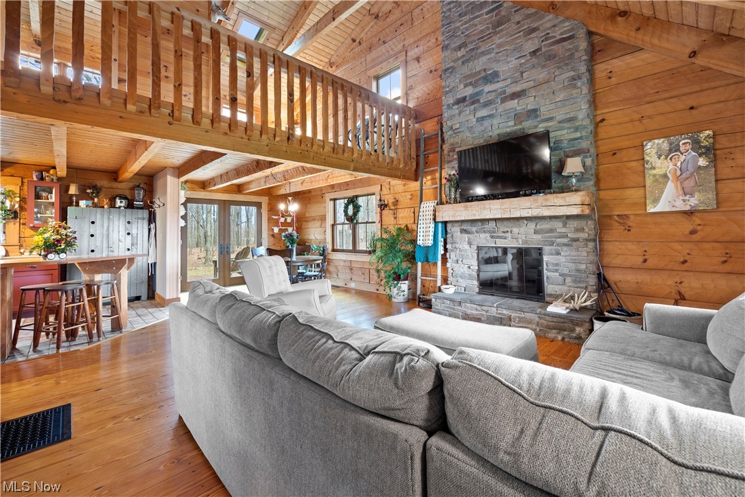 9485 Stone Road Litchfield, OH 44253 - Photo 11 of 50 Living room with wooden walls, a stone fireplace, and beamed ceiling