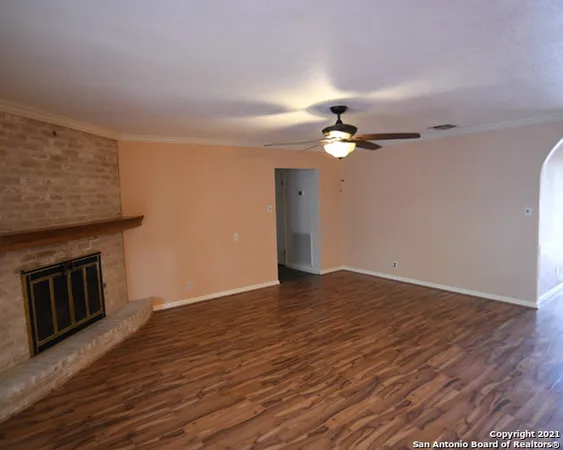 a view of an empty room with wooden floor and a ceiling fan