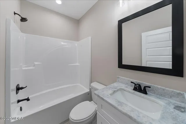 a bathroom with a granite countertop bathtub shower sink vanity mirror and toilet