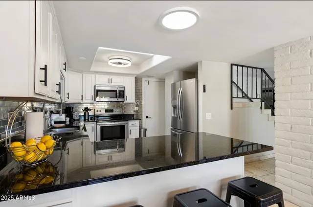 a kitchen with stainless steel appliances granite countertop a refrigerator a stove and white cabinets with wooden floor