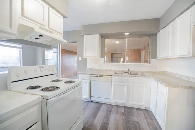 a kitchen with granite countertop a sink stove a refrigerator and white cabinets with wooden floor