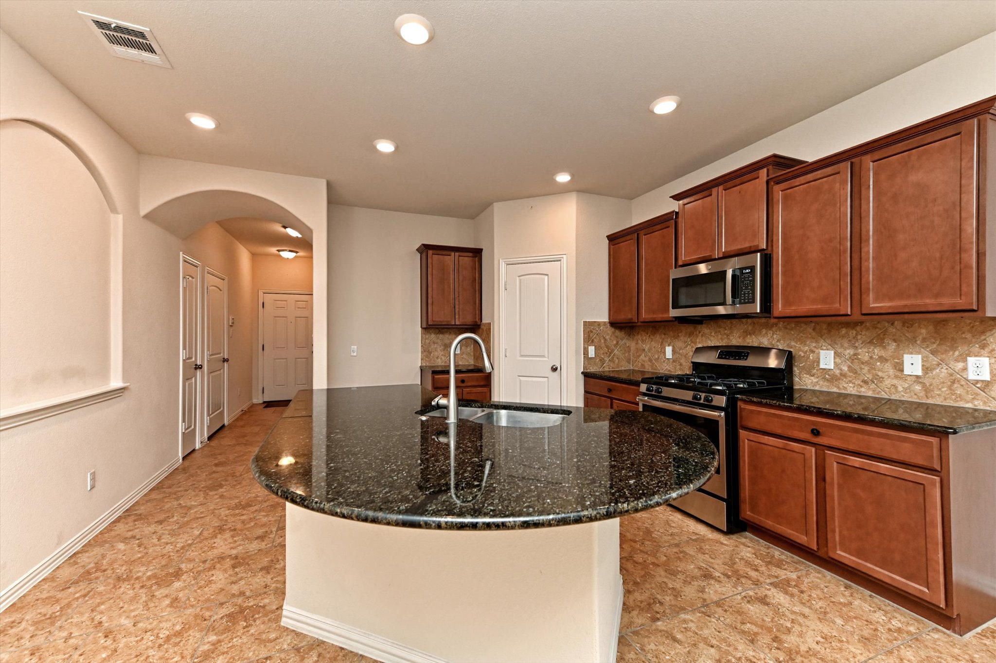 265 Shale Circle Buda, TX 78610 - Photo 6 of 29 Kitchen with arched walkways, stainless steel appliances, dark stone counters, a center island with sink, and recessed lighting
