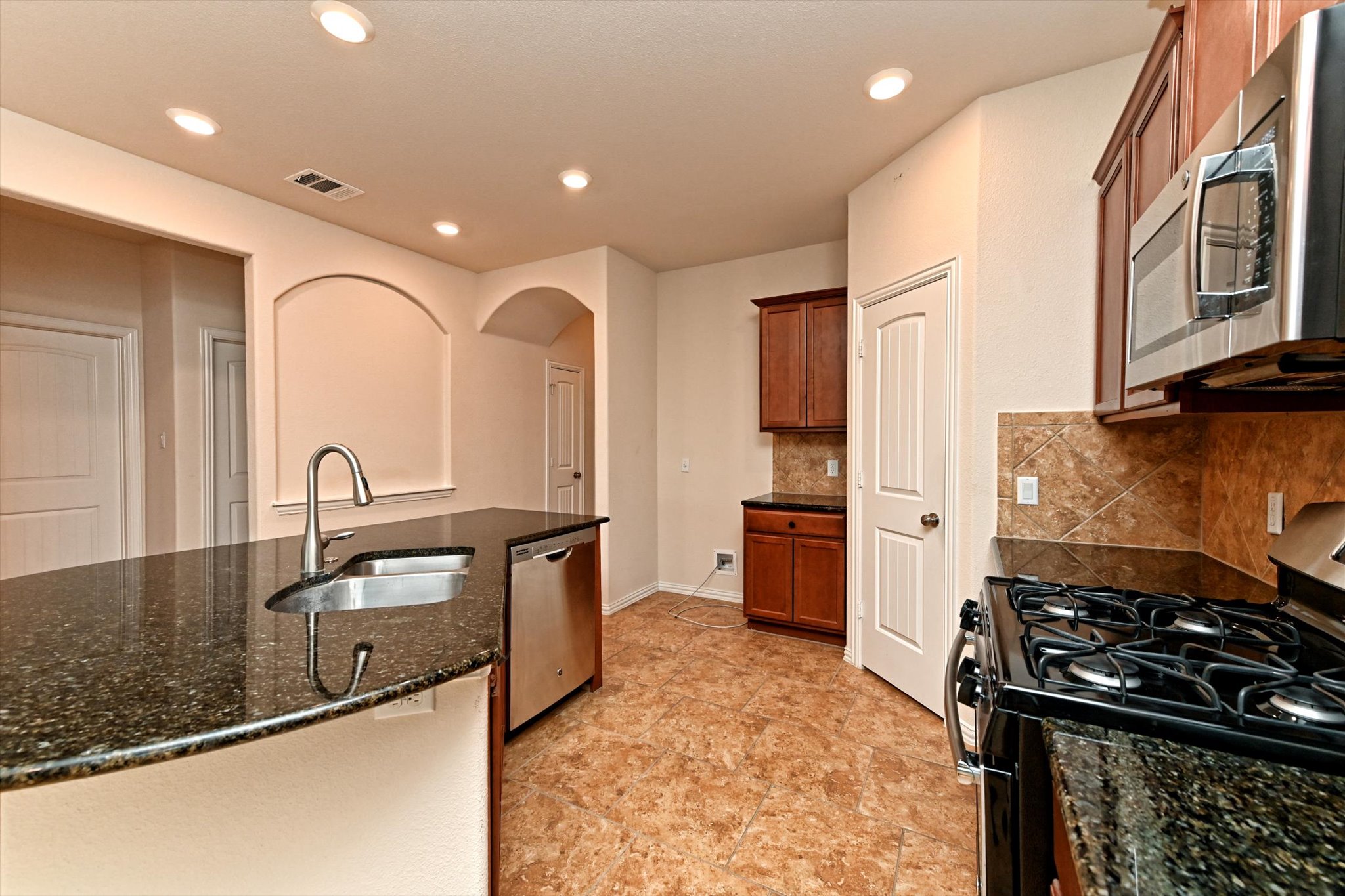 265 Shale Circle Buda, TX 78610 - Photo 8 of 29 Kitchen with stainless steel appliances, dark stone counters, arched walkways, wood finish cabinets, and recessed lighting