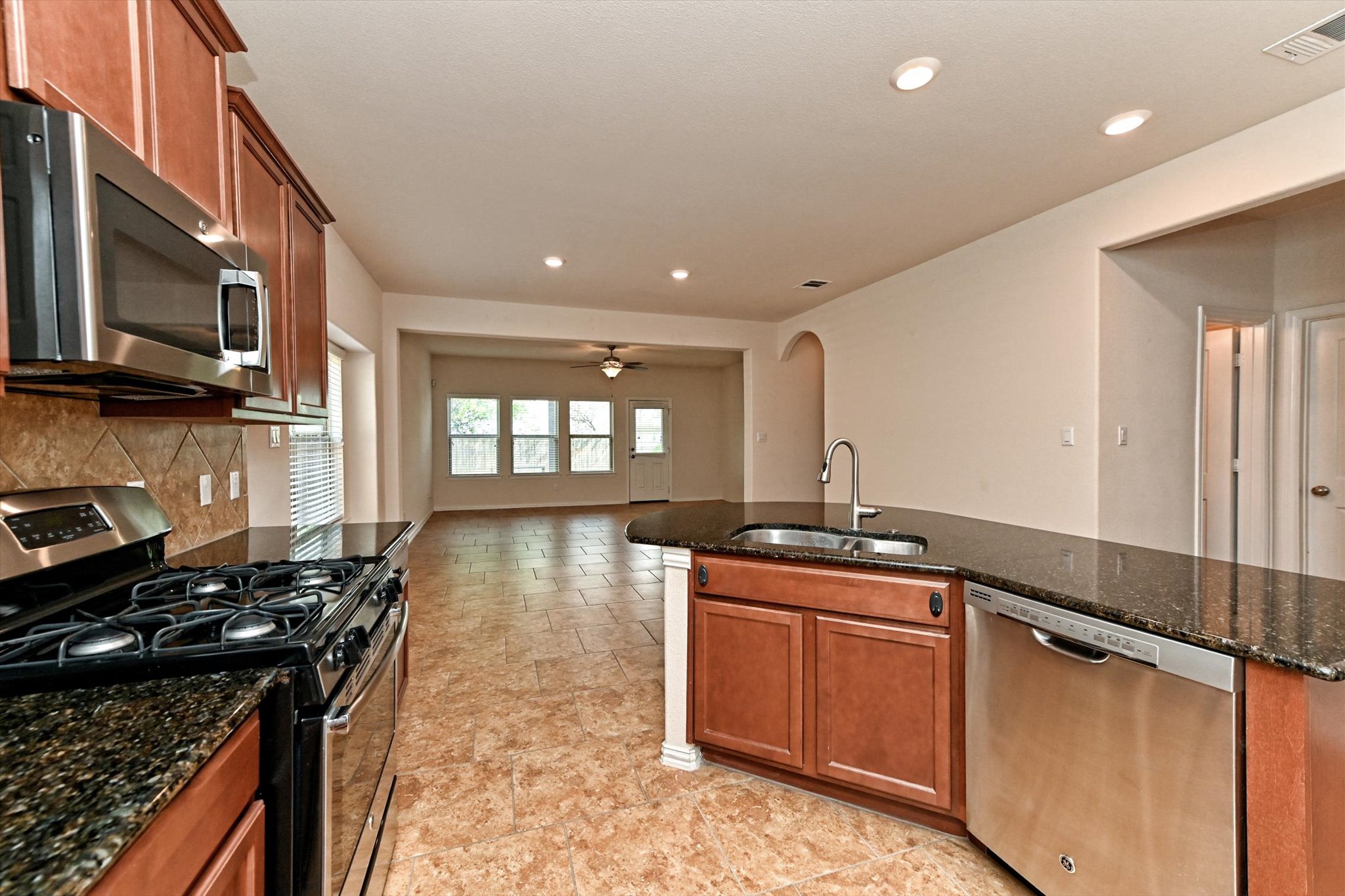 265 Shale Circle Buda, TX 78610 - Photo 9 of 29 Kitchen featuring stainless steel appliances, dark stone countertops, a ceiling fan, arched walkways, and wood finish cabinetry