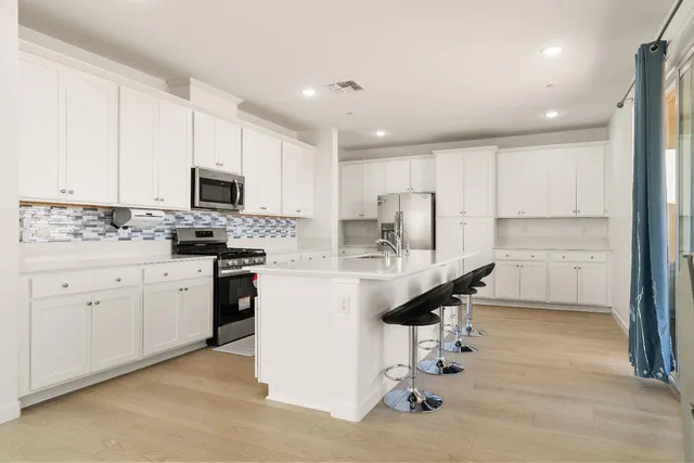 a kitchen with stainless steel appliances kitchen island a refrigerator a stove a sink and chairs