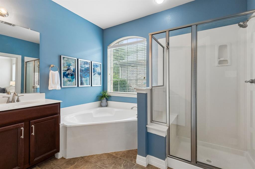960 Remuda Road Frisco, TX 75033 - Photo 19 of 39 Bathroom featuring a glass-enclosed shower, built-in bathtub, arched window with blinds, dark wood vanity with a white countertop, and tiled flooring