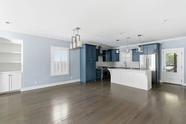 a kitchen with stainless steel appliances kitchen island granite countertop a refrigerator a stove and white cabinets with wooden floor