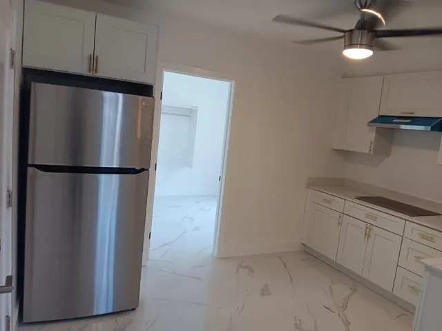 a view of a refrigerator in kitchen and an empty room with wooden floor cabinets