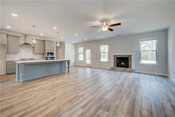 an empty room with wooden floor a ceiling fan and kitchen view