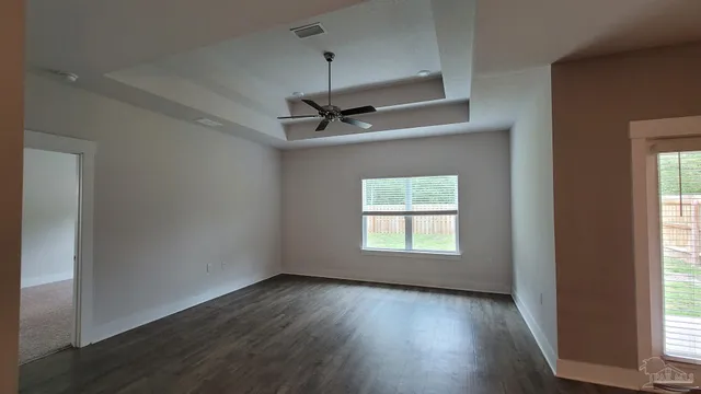 an empty room with wooden floor windows and fan