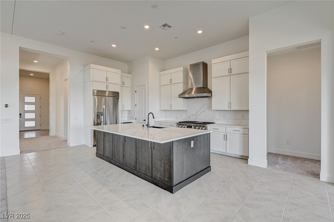 4992 Ascent Point Las Vegas, NV 89135 - Photo 20 of 61 Kitchen featuring backsplash, wall chimney range hood, white cabinets, a kitchen island with sink, and light tile patterned floors