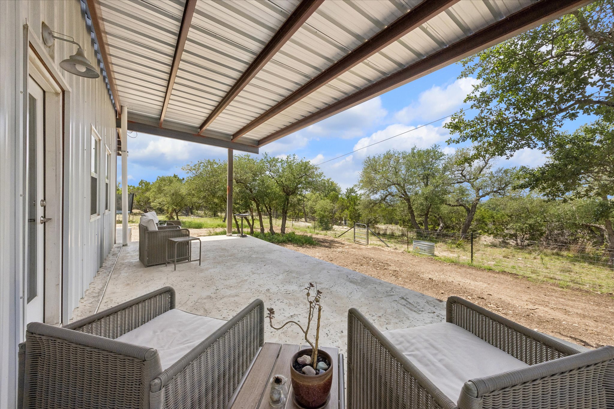 6411 West Fitzhugh Road Dripping Springs, TX 78620 - Photo 7 of 34 Expansive concrete patio beneath a corrugated metal roof extension, providing a generous outdoor area