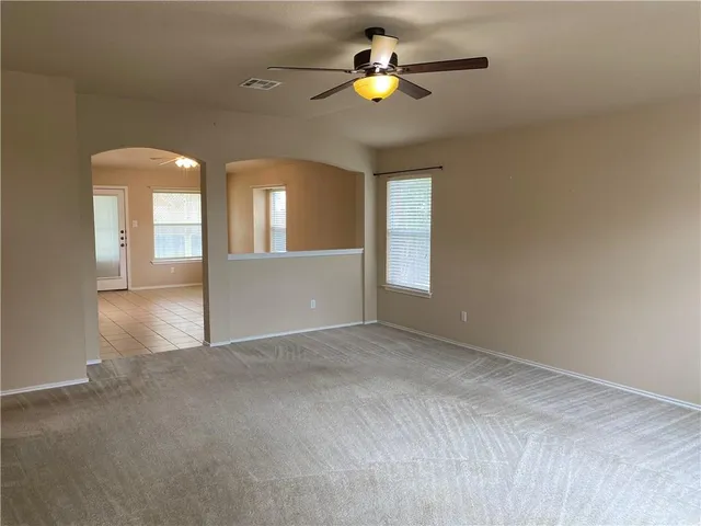an empty room with chandelier fan and windows