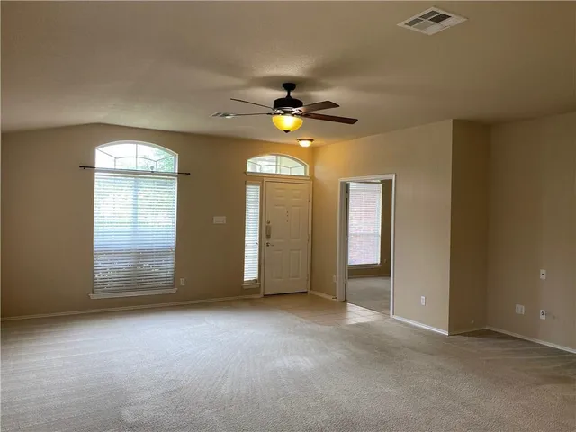 an empty room with chandelier fan and windows