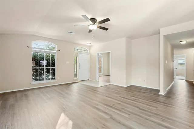 a view of an empty room with wooden floor and a ceiling fan