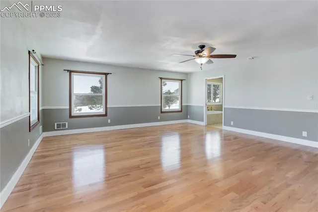 an empty room with chandelier fan and windows