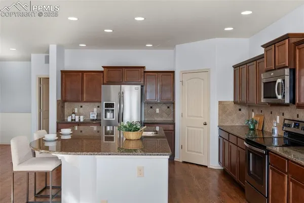 a kitchen with stainless steel appliances granite countertop a refrigerator a sink a stove a oven a dining table and chairs with wooden floor