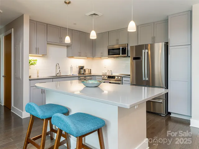 a kitchen with stainless steel appliances a sink a stove a refrigerator white cabinets and wooden floor