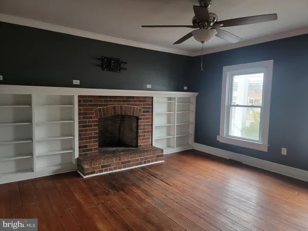an empty room with wooden floor fire place and windows