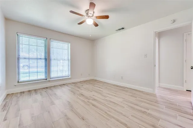 an empty room with wooden floor chandelier fan and windows