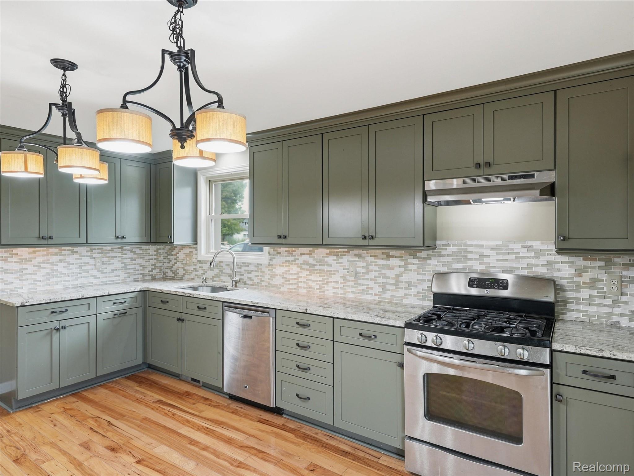 117 Kenyon Road Algonac, MI 48001 - Photo 19 of 47 Kitchen featuring hardwood flooring, green shaker-style cabinetry, mosaic tile backsplash, and stainless steel appliances including a gas range and dishwasher