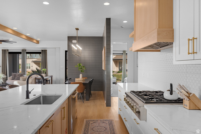 5367 Cyan Lane St. George, UT 84790 - Photo 24 of 49 Gourmet kitchen with white countertops, a large island featuring an undermount sink and matte black faucet, a built-in range, a light wood-finish range hood, and white cabinetry with brass hardware