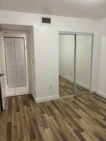 a view of an empty room with wooden floor and a bathroom