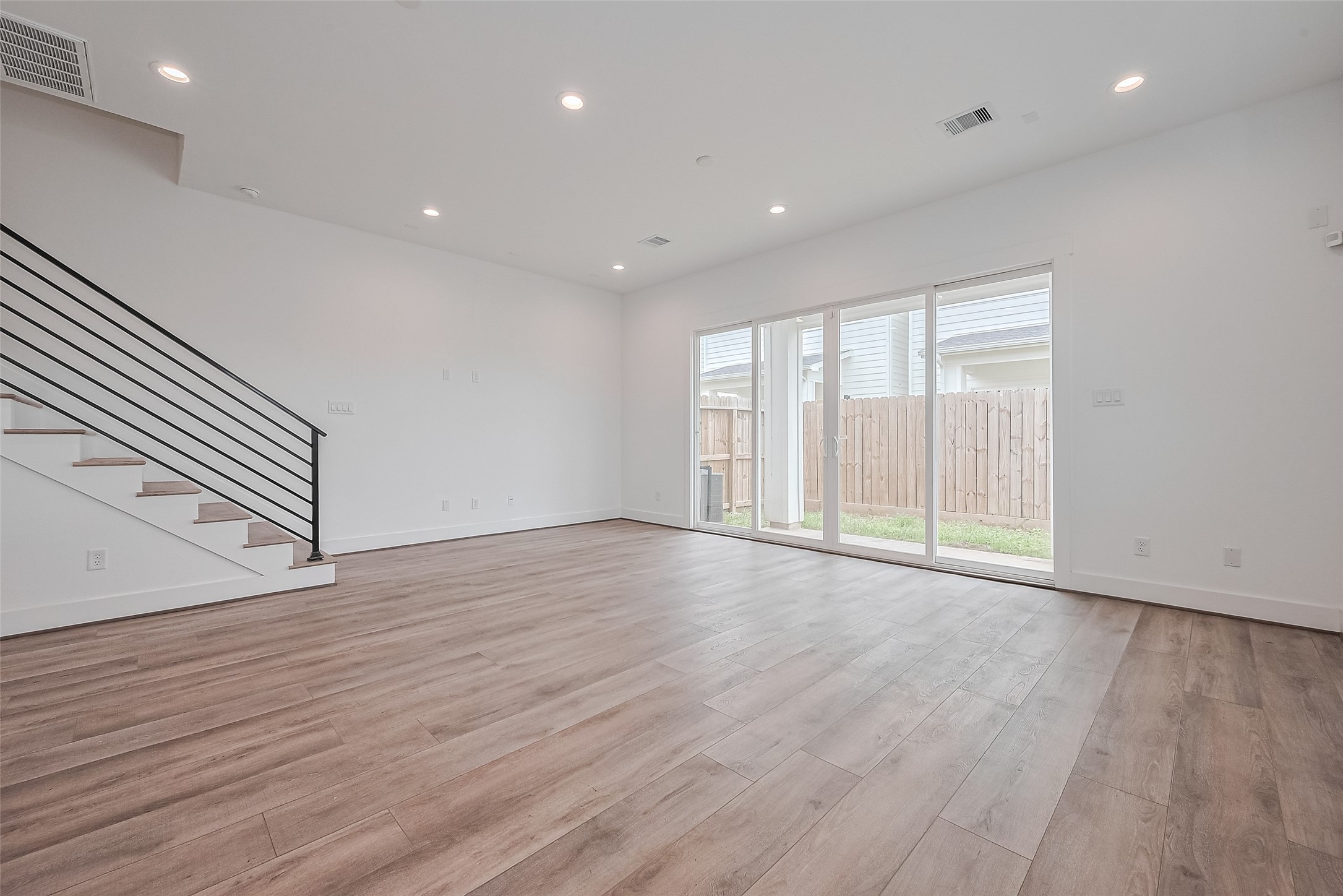 3510 Hadley Street Houston, TX 77004 - Photo 11 of 48 Anchored by warm-toned wood flooring, the spacious living room is bathed in natural light from sliding glass doors that lead to the backyard. A staircase with bold lines adds architectural interest to the space.