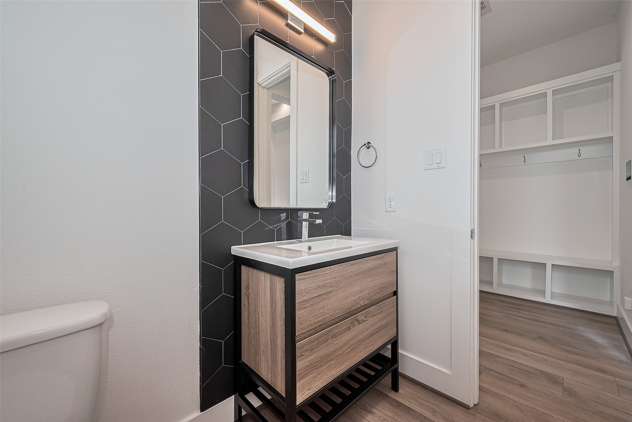 3510 Hadley Street Houston, TX 77004 - Photo 21 of 48 This chic half bath stands out with its black textured accent wall and streamlined vanity. Just outside, a practical mudroom with hooks, cubbies, and shelving offers a perfect drop zone for everyday essentials.