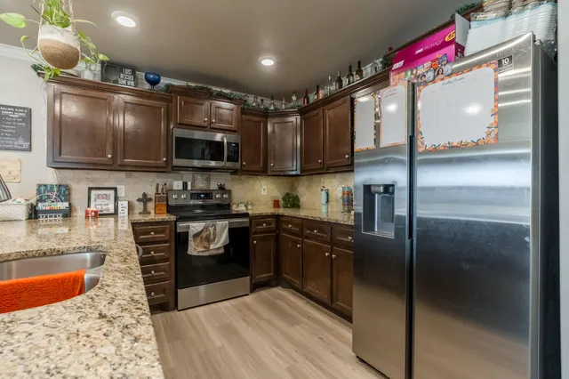 a kitchen with stainless steel appliances granite countertop a refrigerator a stove and a sink with wooden floor