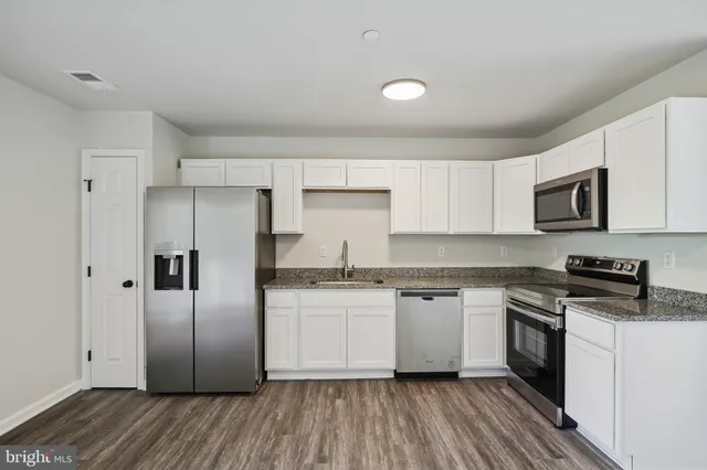 a kitchen with granite countertop a refrigerator stove a sink and white cabinets with wooden floor