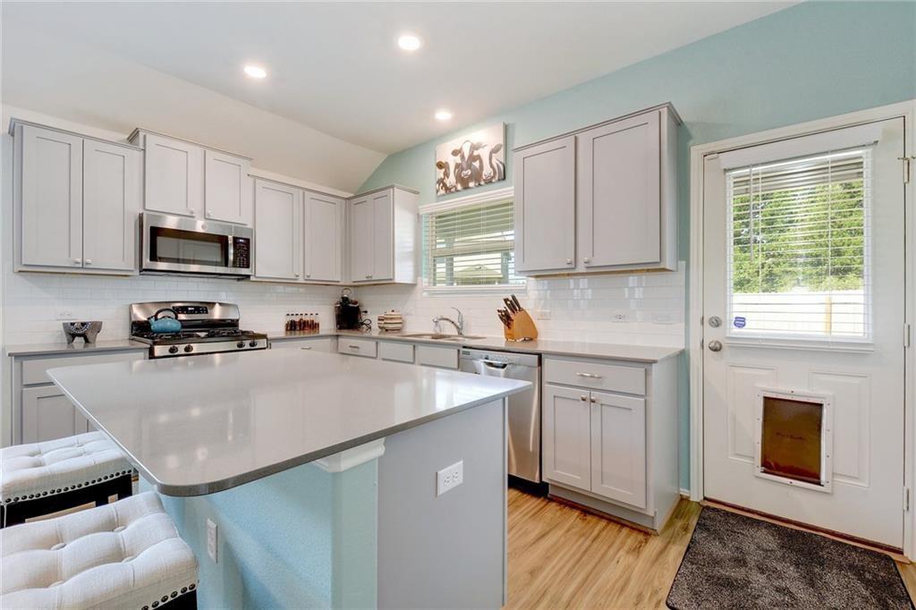 6813 Colorado Bluffs Road Austin, TX 78744 - Photo 5 of 20 Kitchen featuring a kitchen bar, stainless steel appliances, a center island, light wood-style flooring, and gray cabinets