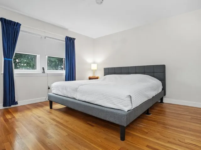 a bedroom with a bed lamp on desk and a window