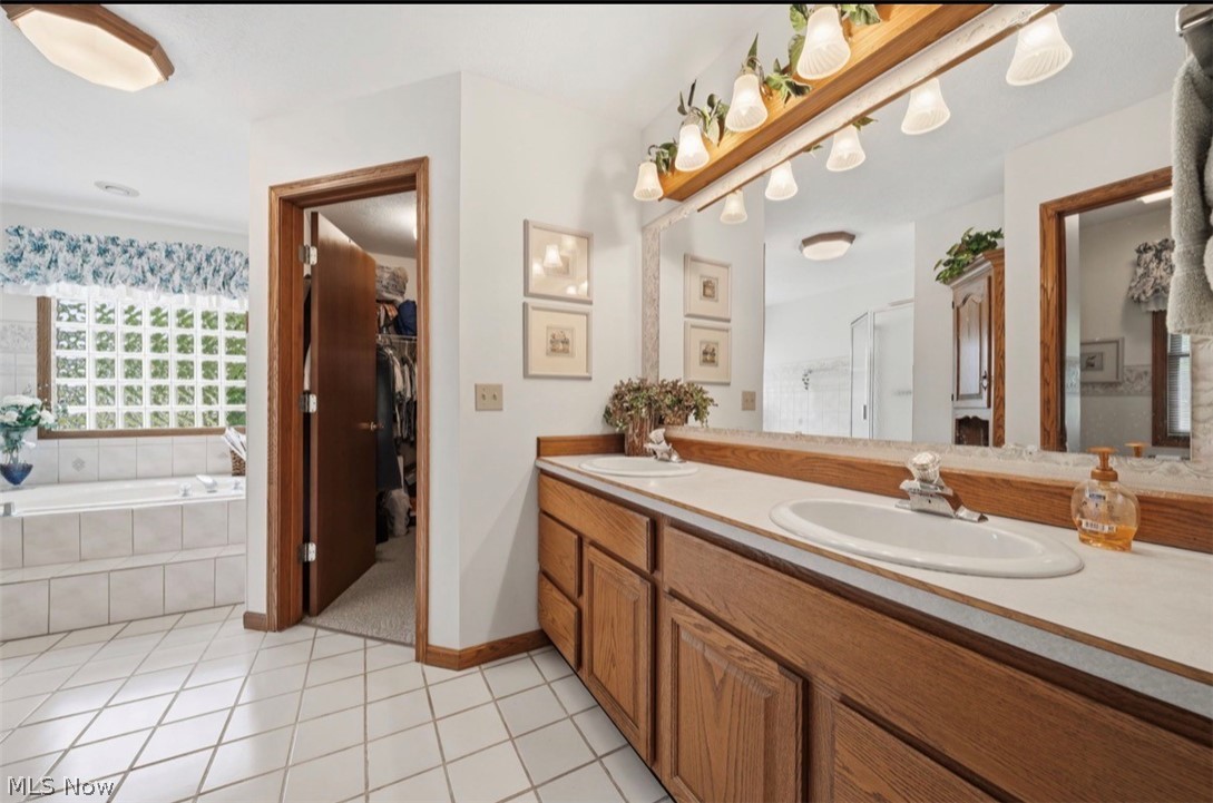 3556 Lake Road Conneaut, OH 44030 - Photo 29 of 39 Dual vanity with wood cabinetry and an integrated countertop, large mirror with decorative lighting, white tile flooring, and a jetted tub alcove with a lattice-patterned window