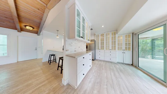 a large white kitchen with wide window and wooden floor