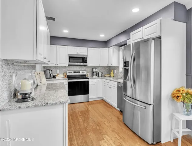 a kitchen with granite countertop a refrigerator a sink a stove top oven and cabinets