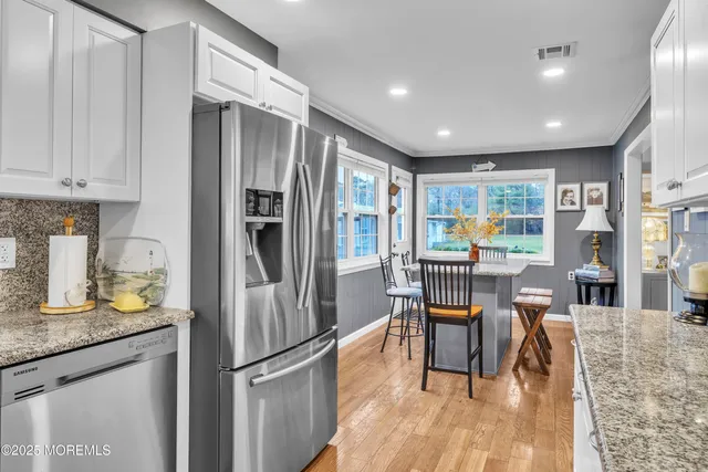 a kitchen with stainless steel appliances granite countertop a refrigerator a stove a sink a dining table and chairs with wooden floor