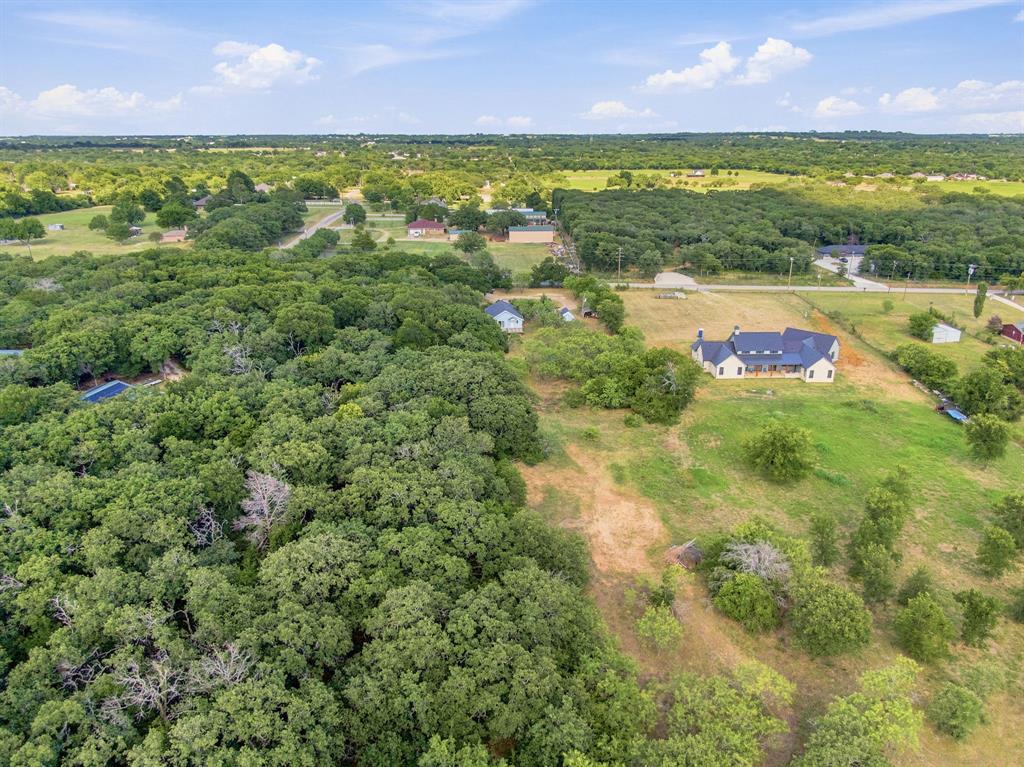 3325 Dove Creek Road Cleburne, TX 76031 - Photo 34 of 40 Expansive property featuring a modern residence with a dark roof and light-toned siding, set amidst open green spaces and dense tree coverage