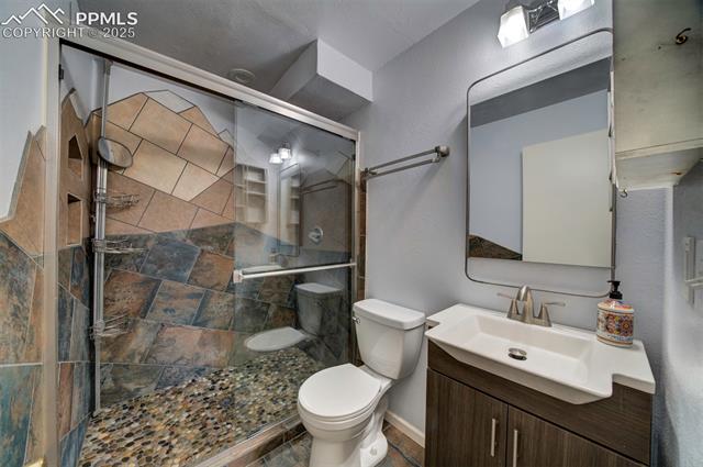 3870 Half Turn Road Colorado Springs, CO 80917 - Photo 32 of 34 Full bathroom featuring toilet, a shower stall, vanity, stone finish flooring, and baseboards