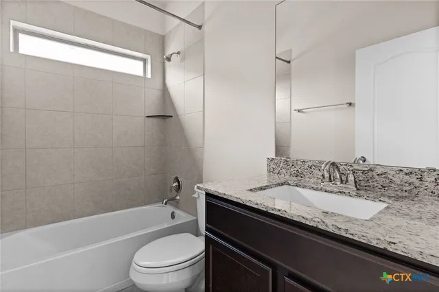 a bathroom with a granite countertop bathtub shower sink vanity mirror and toilet
