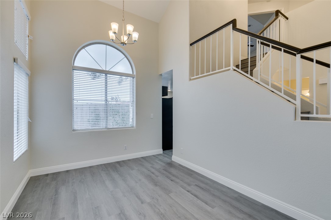 1738 Toltec Circle Henderson, NV 89014 - Photo 31 of 46 A graceful staircase ascends from a room with elegant wood flooring and a striking arched window, bathed in soft illumination from a central chandelier.