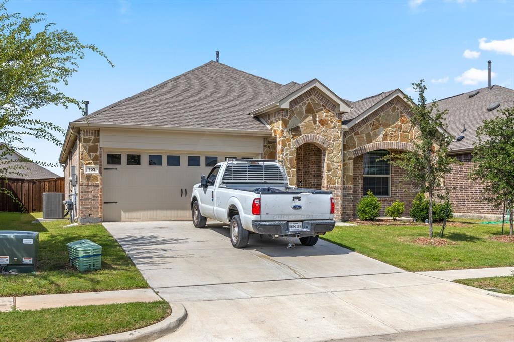 French country home with stone siding, concrete driveway, an attached garage, roof with shingles, and brick siding