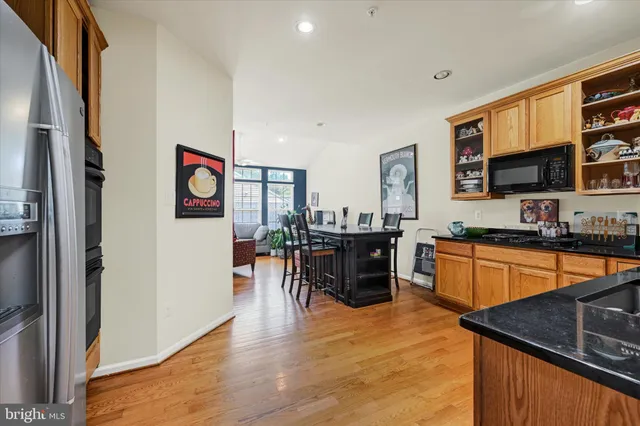 a open kitchen with stainless steel appliances granite countertop a stove top oven a sink a dining table and chairs with wooden floor