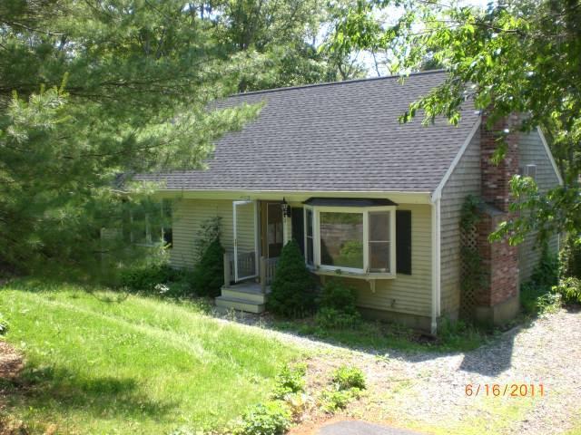 a view of a brick house with a yard plants and large tree